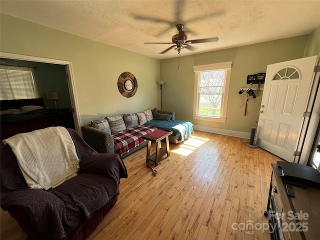 living area featuring light wood finished floors, ceiling fan, baseboards, and a textured ceiling