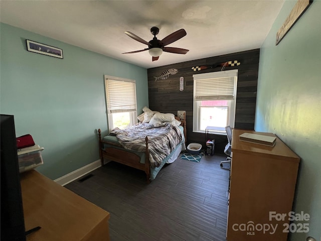 bedroom featuring wooden walls, dark wood-type flooring, a ceiling fan, and baseboards