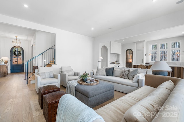 living room featuring arched walkways, recessed lighting, an inviting chandelier, light wood-type flooring, and stairs