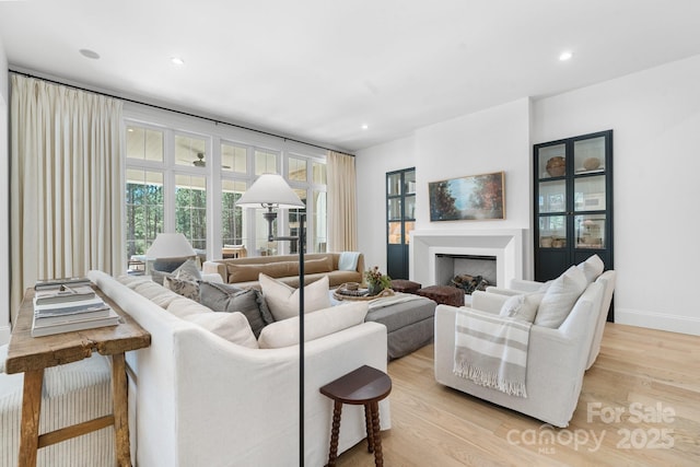 living room featuring light wood-style floors, a fireplace, baseboards, and recessed lighting