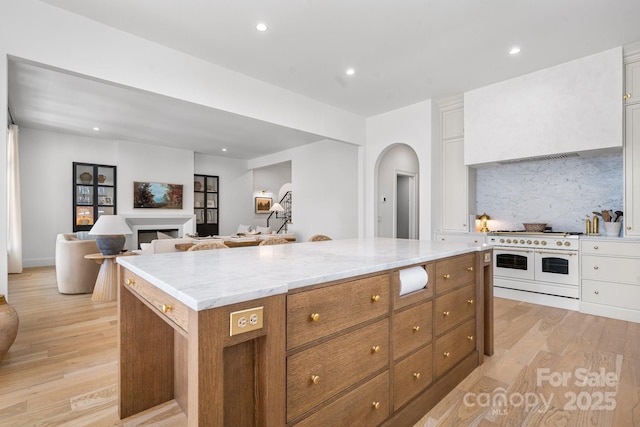 kitchen with range with two ovens, a kitchen island, brown cabinets, open floor plan, and white cabinetry