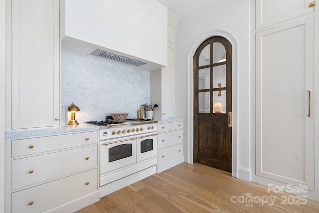 kitchen featuring range with two ovens, light countertops, decorative backsplash, light wood-style floors, and wall chimney exhaust hood