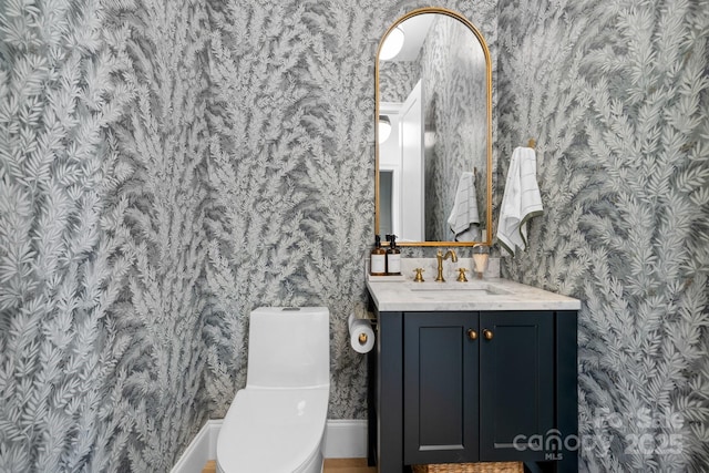 bathroom featuring toilet, wallpapered walls, and vanity