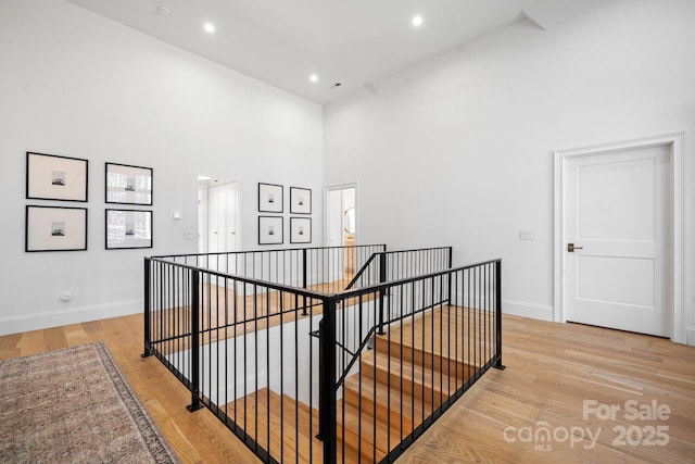 hall featuring baseboards, a high ceiling, light wood finished floors, and an upstairs landing