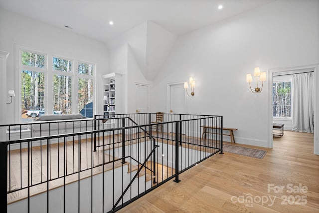 corridor with light wood-style flooring, recessed lighting, a high ceiling, an upstairs landing, and baseboards