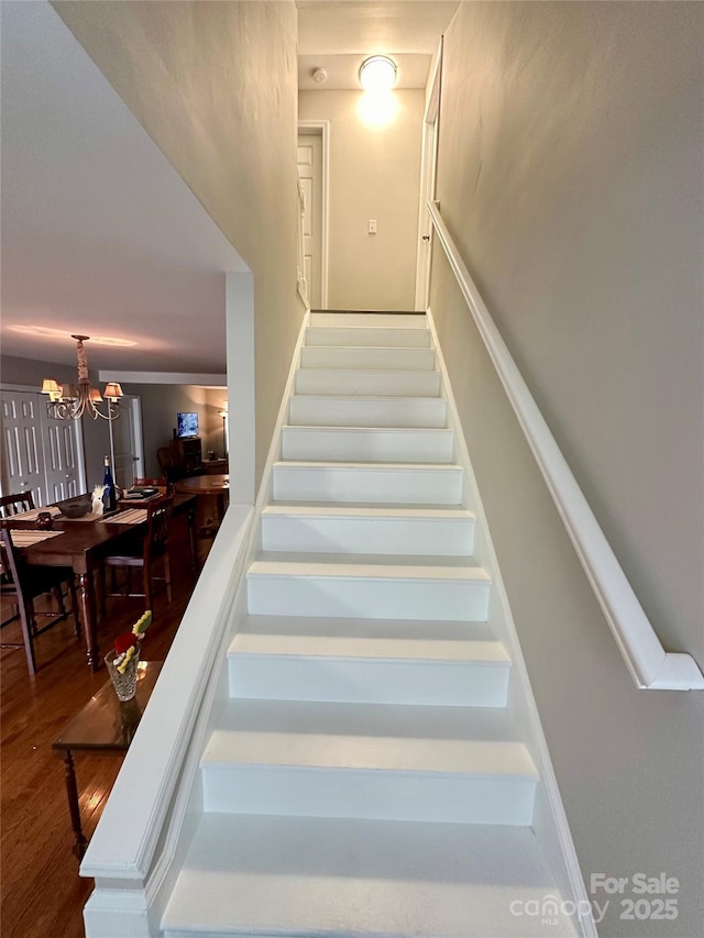 stairs with hardwood / wood-style flooring and an inviting chandelier