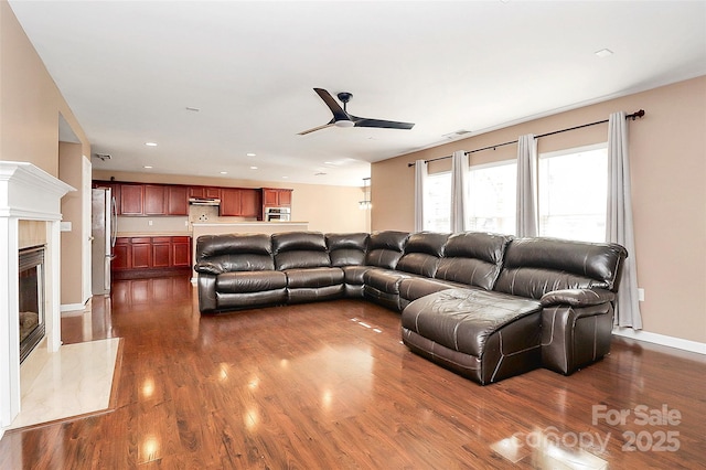 living room featuring dark wood-type flooring, visible vents, a fireplace, and ceiling fan