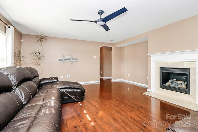 living room with a high end fireplace, ceiling fan, baseboards, and wood finished floors