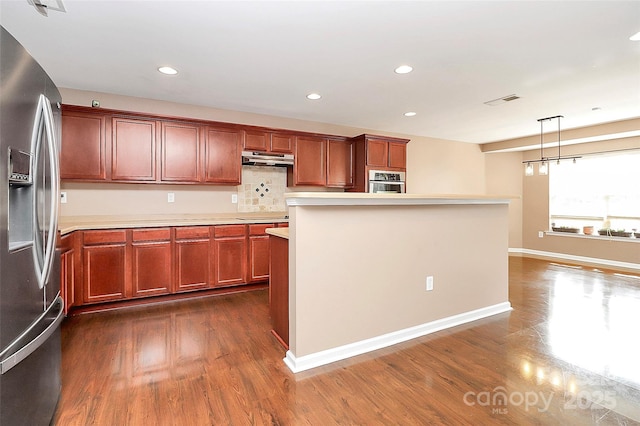 kitchen with dark wood finished floors, stainless steel appliances, visible vents, light countertops, and under cabinet range hood