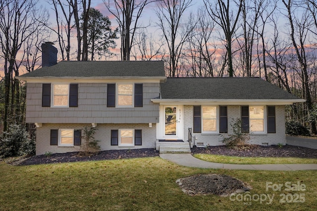 tri-level home with a chimney, a lawn, and brick siding