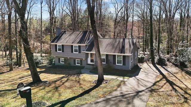 tri-level home featuring a front lawn, a chimney, a shingled roof, and aphalt driveway