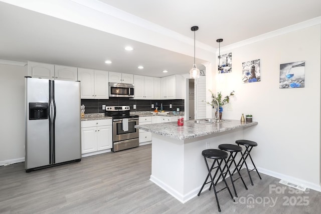 kitchen featuring white cabinets, a breakfast bar area, a peninsula, hanging light fixtures, and stainless steel appliances