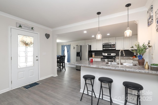 kitchen with a peninsula, appliances with stainless steel finishes, a sink, and white cabinets