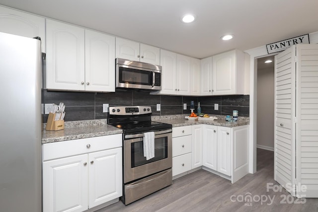 kitchen with stainless steel appliances, backsplash, light wood-style floors, white cabinets, and light stone countertops