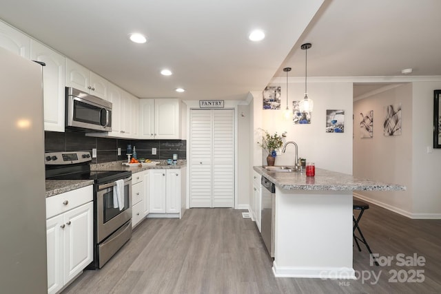 kitchen with pendant lighting, stainless steel appliances, white cabinetry, a sink, and a kitchen bar