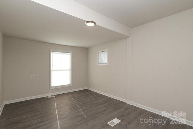 empty room with dark wood-style floors, visible vents, and baseboards