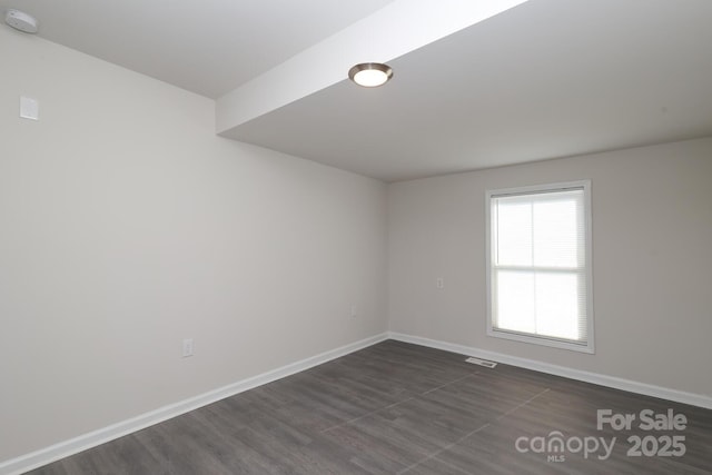 spare room with dark wood-type flooring, visible vents, and baseboards