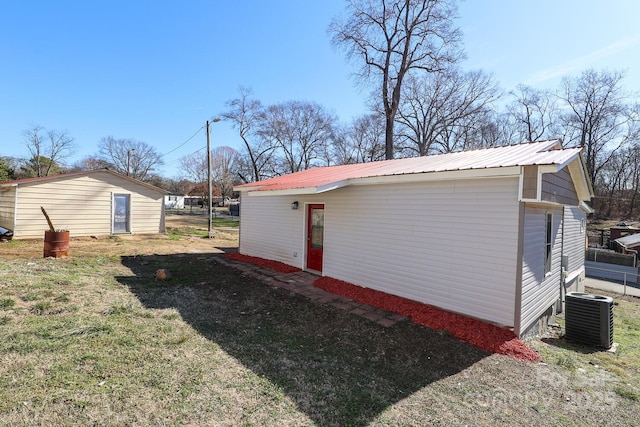 view of property exterior featuring metal roof, a lawn, an outdoor structure, and cooling unit