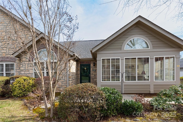 view of front of property with stone siding and roof with shingles