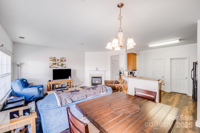 dining space with a notable chandelier, visible vents, wood finished floors, and a glass covered fireplace