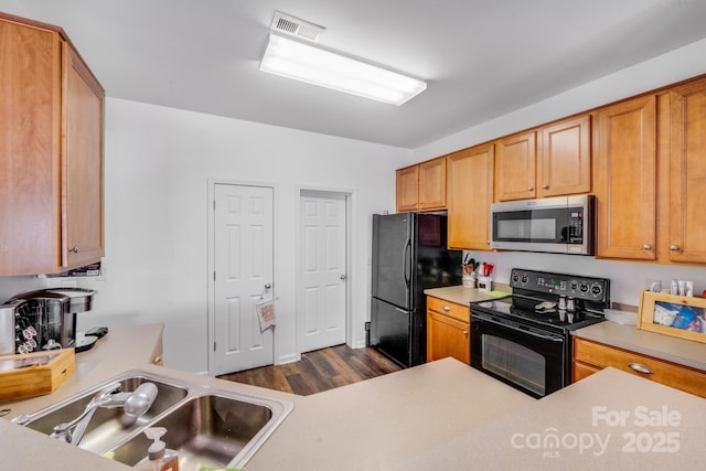 kitchen with a sink, black appliances, light countertops, and visible vents