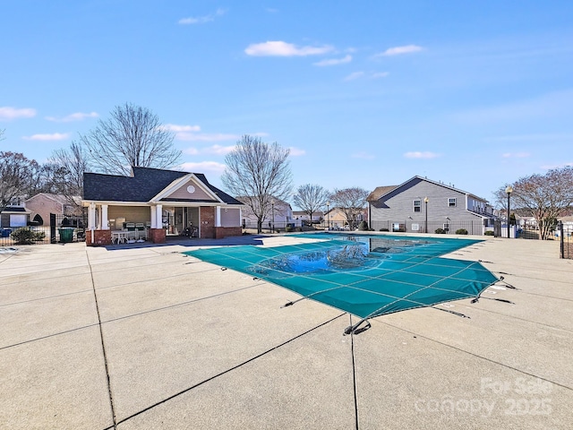 community pool with a patio area, fence, and a residential view