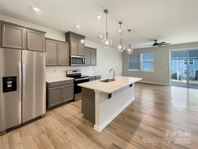 kitchen with sink, decorative light fixtures, stainless steel appliances, gray cabinets, and an island with sink