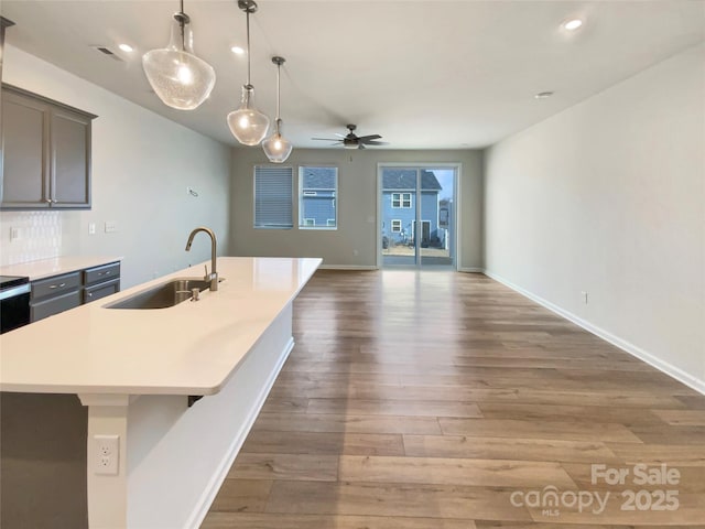 kitchen with hardwood / wood-style floors, sink, decorative light fixtures, ceiling fan, and a kitchen island with sink