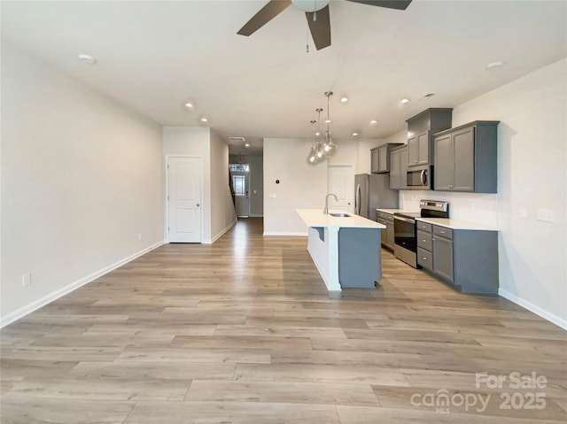 kitchen with a center island with sink, gray cabinetry, hanging light fixtures, sink, and appliances with stainless steel finishes