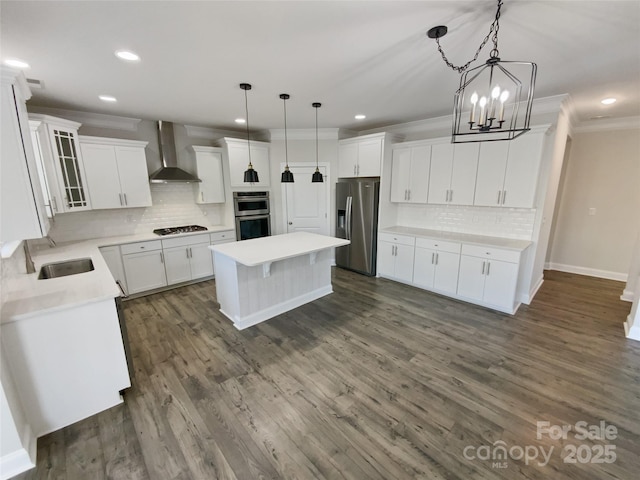 kitchen with appliances with stainless steel finishes, wall chimney exhaust hood, pendant lighting, and white cabinets