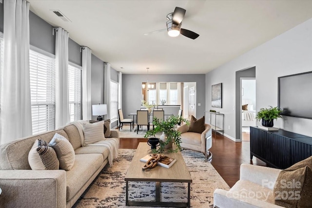 living room with ceiling fan with notable chandelier, baseboards, visible vents, and dark wood-style flooring