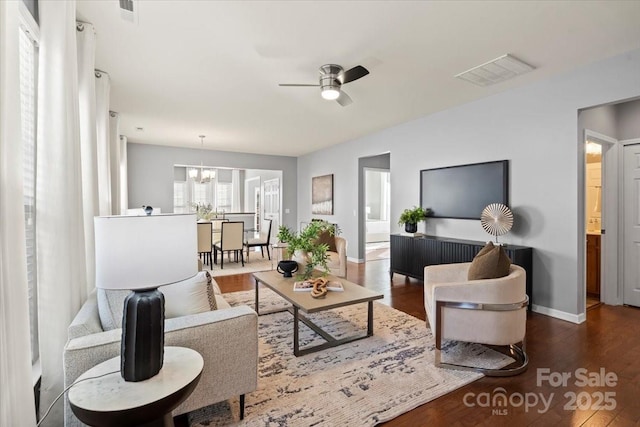 living area featuring ceiling fan with notable chandelier, baseboards, wood finished floors, and visible vents
