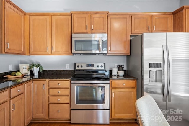 kitchen with brown cabinets, dark stone countertops, and stainless steel appliances