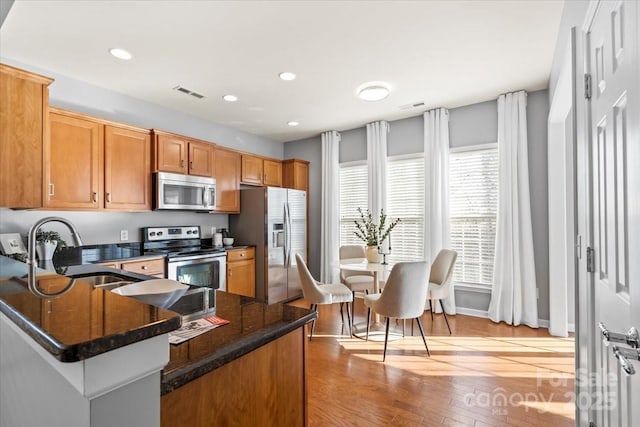 kitchen with dark stone counters, a sink, light wood-style floors, appliances with stainless steel finishes, and visible vents