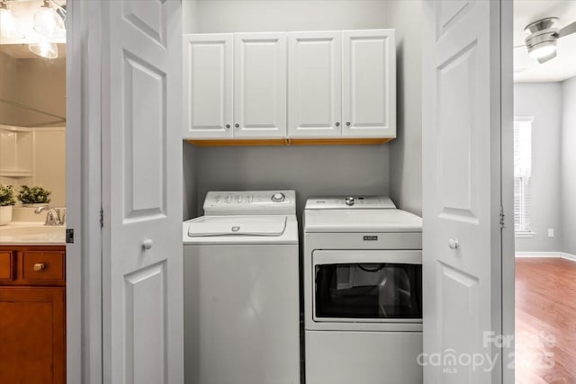 clothes washing area featuring separate washer and dryer, wood finished floors, a sink, and cabinet space
