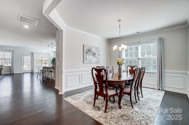 dining space with dark wood finished floors, a notable chandelier, visible vents, ornamental molding, and wainscoting