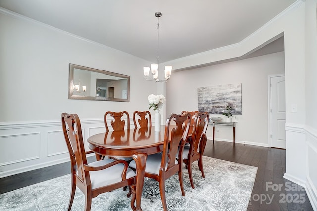 dining space featuring a wainscoted wall, dark wood finished floors, a decorative wall, an inviting chandelier, and ornamental molding