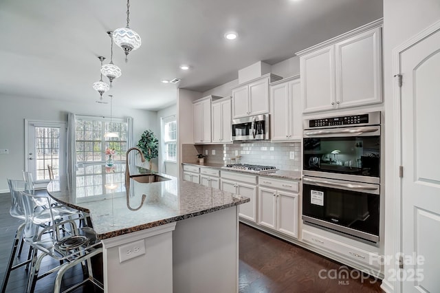 kitchen featuring hanging light fixtures, appliances with stainless steel finishes, light stone counters, and a sink