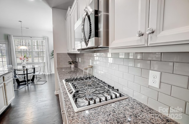 kitchen featuring white cabinets, appliances with stainless steel finishes, light stone counters, pendant lighting, and backsplash