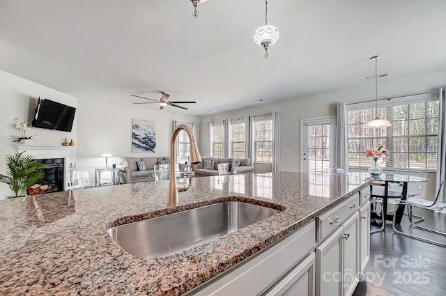 kitchen with stone counters, pendant lighting, open floor plan, white cabinets, and a sink