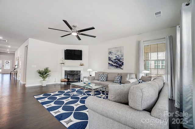 living room featuring dark wood-style floors, a wealth of natural light, a glass covered fireplace, and visible vents