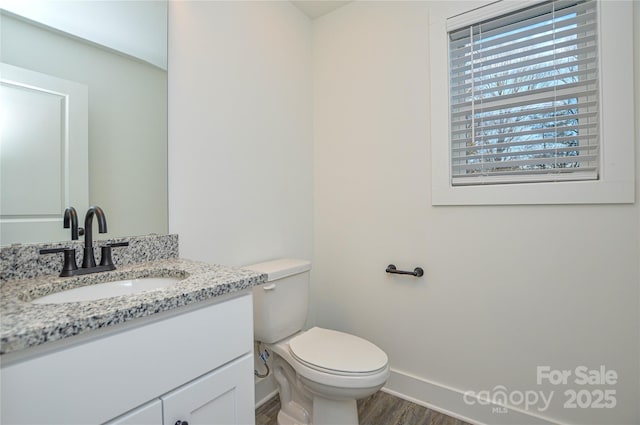 half bath with baseboards, vanity, toilet, and wood finished floors