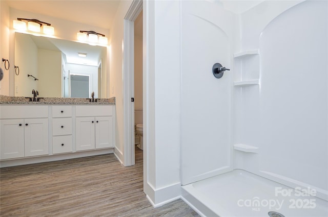 bathroom with toilet, a sink, wood finished floors, a shower stall, and double vanity