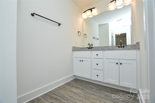 bathroom with double vanity, a sink, baseboards, and wood finished floors