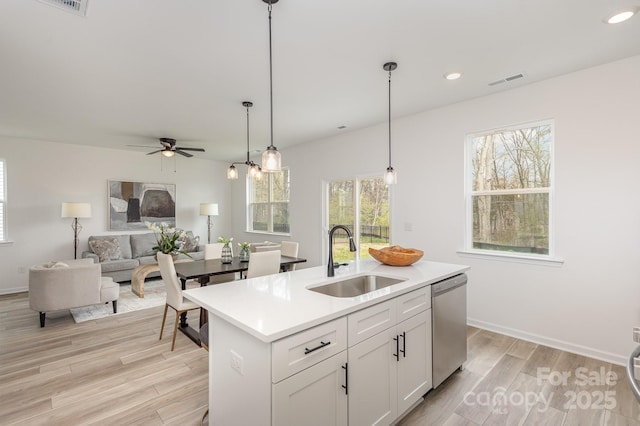 kitchen with a center island with sink, light countertops, white cabinets, a sink, and dishwasher