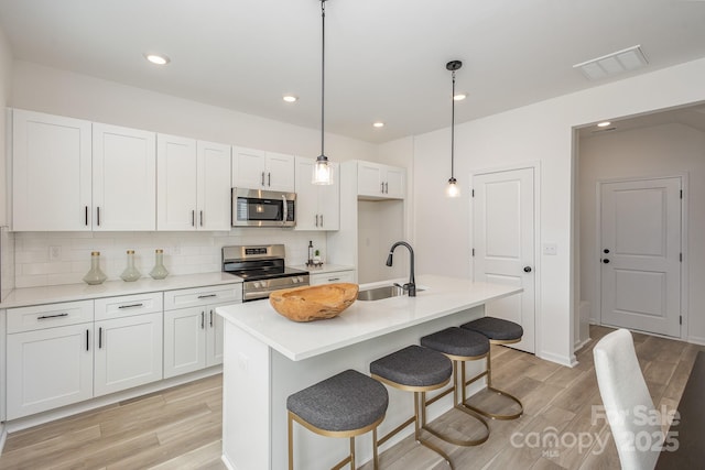 kitchen with stainless steel appliances, light countertops, and an island with sink