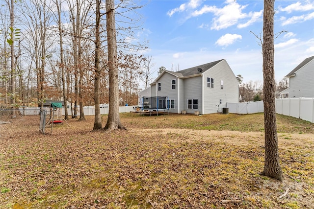 back of house featuring a fenced backyard, a trampoline, central AC unit, and a yard