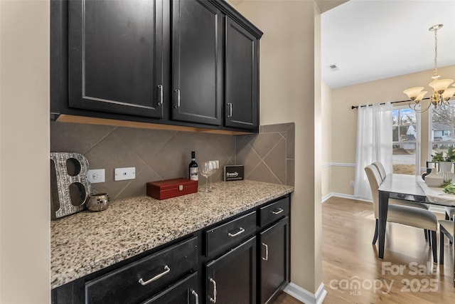 kitchen featuring tasteful backsplash, baseboards, dark cabinets, a chandelier, and pendant lighting