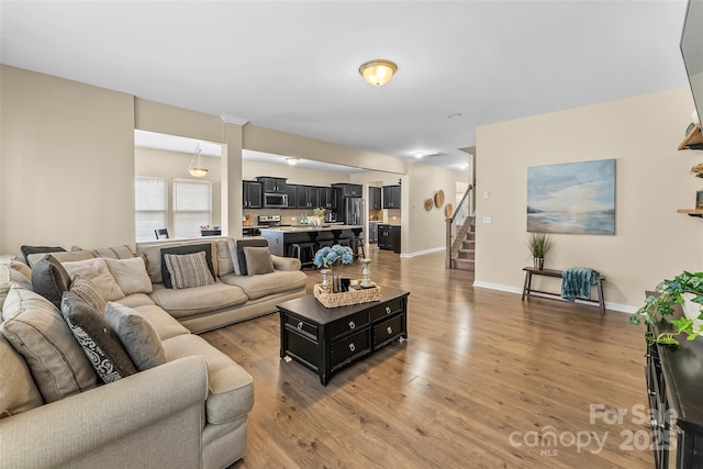 living room with light wood-type flooring, stairs, and baseboards