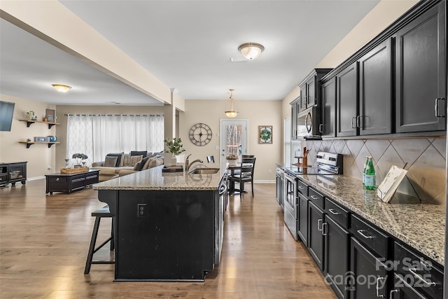 kitchen with a kitchen island with sink, open floor plan, appliances with stainless steel finishes, dark cabinetry, and pendant lighting